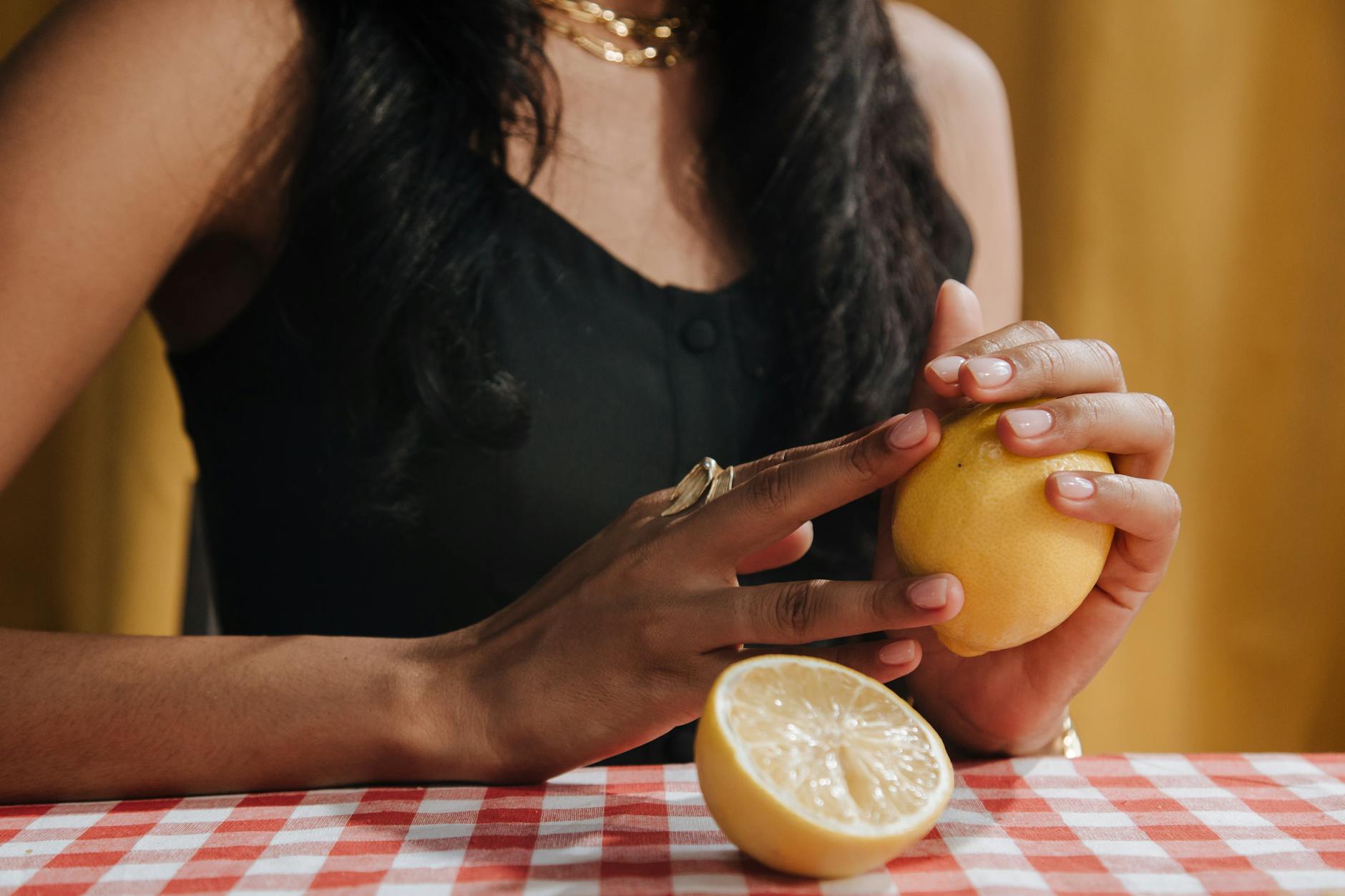 Hand holding a fresh lemon on soft pink background with additional lemons, symbolizing renewal and sensitivity