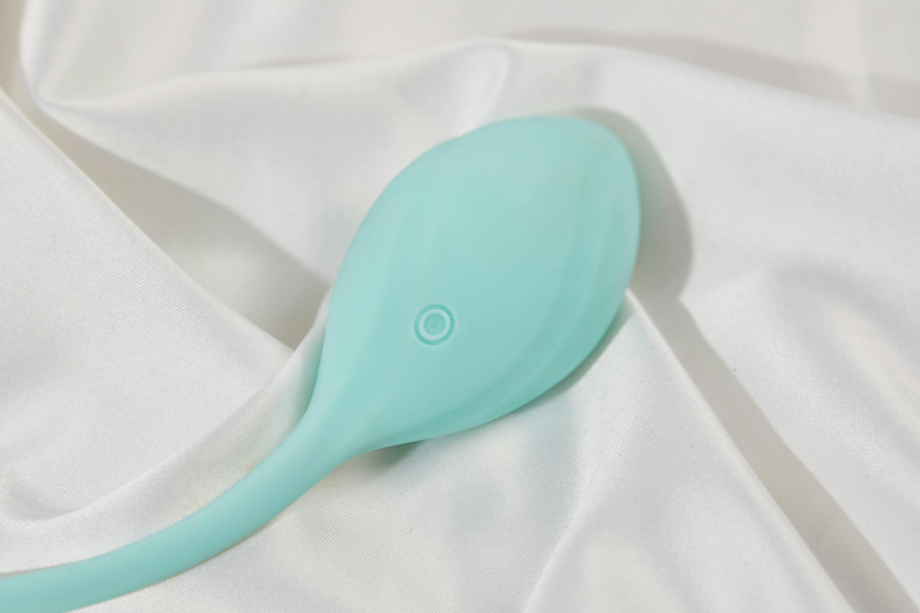 A stylish teal vibrator on smooth white silk fabric, perfect for understanding different toy textures and materials.