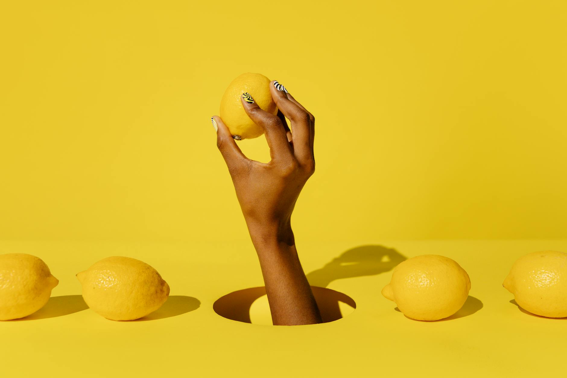Hand holding a fresh lemon against a vivid yellow background