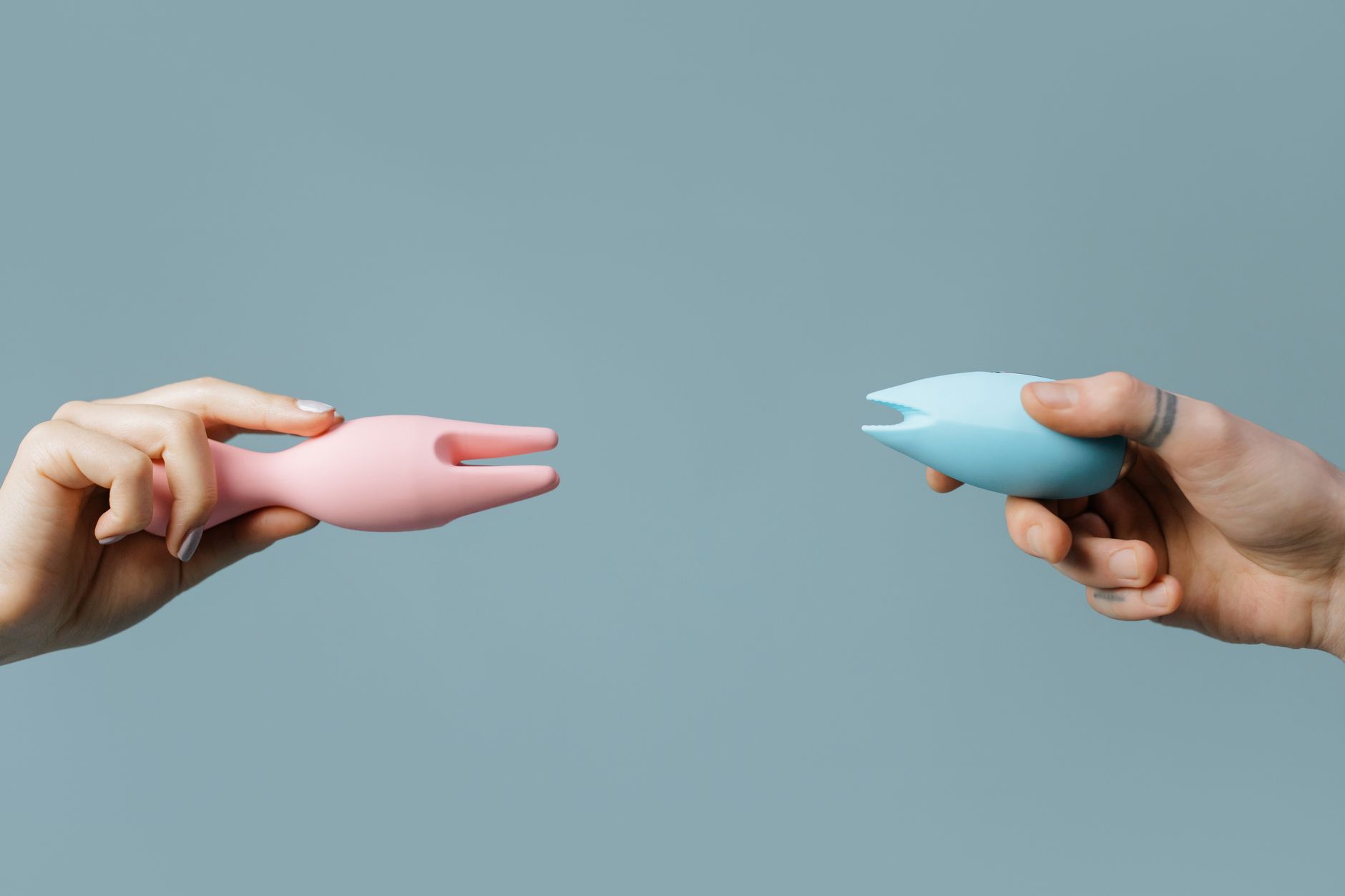Hands holding colorful lemon vibrators and clitoral vibrators against a soft pastel background