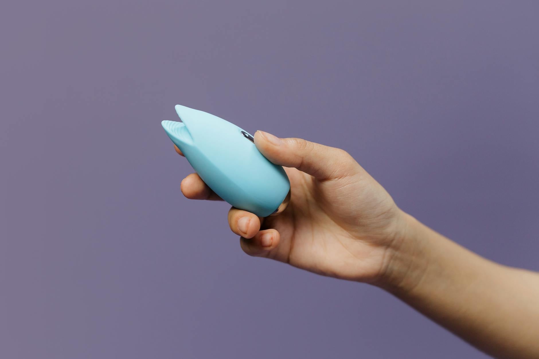 A hand holds a blue silicone lemon vibrator against a purple background, symbolizing pleasure and sexual wellness.
