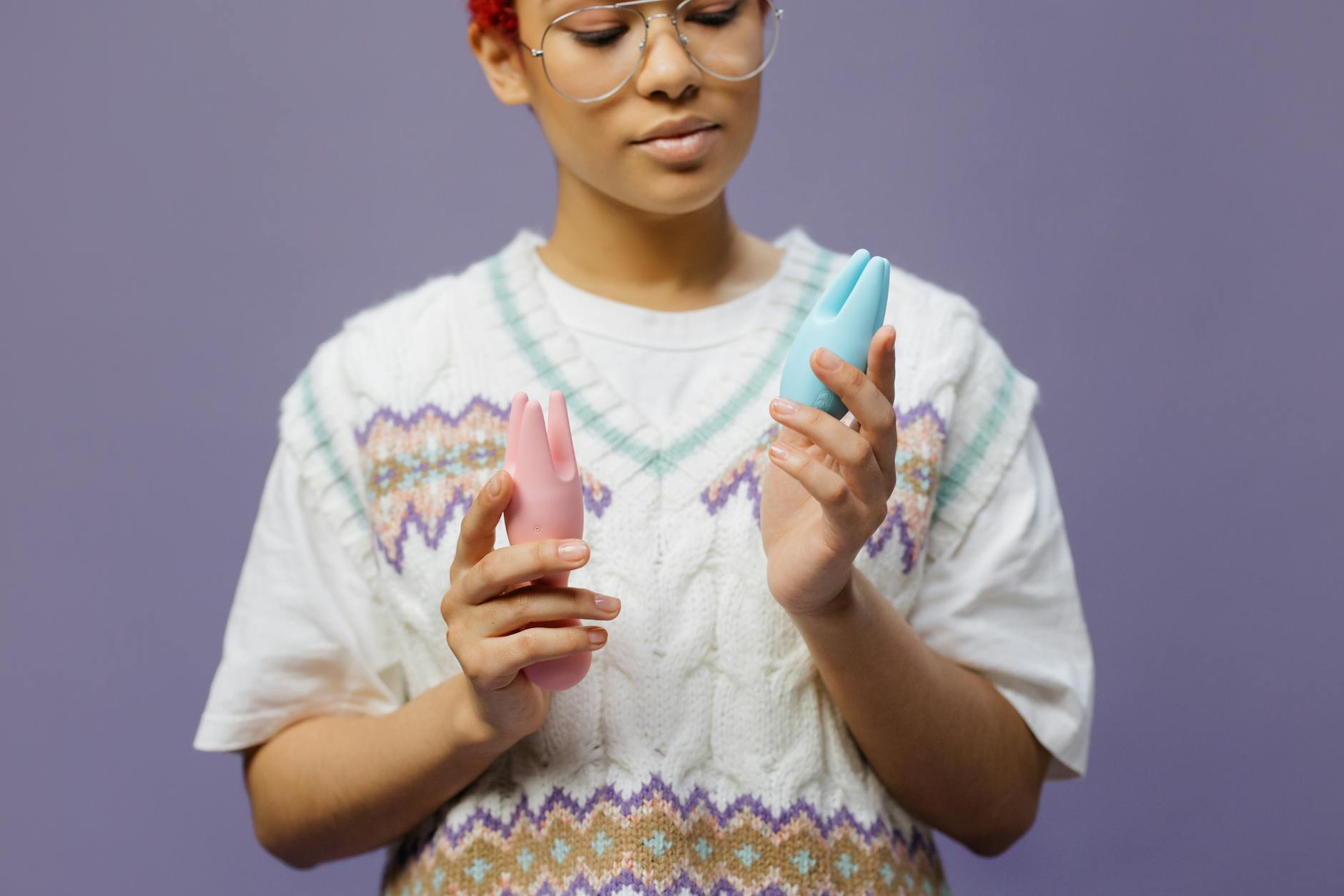 Woman holding blue and pink clitoral vibrators, considering different options for pleasure