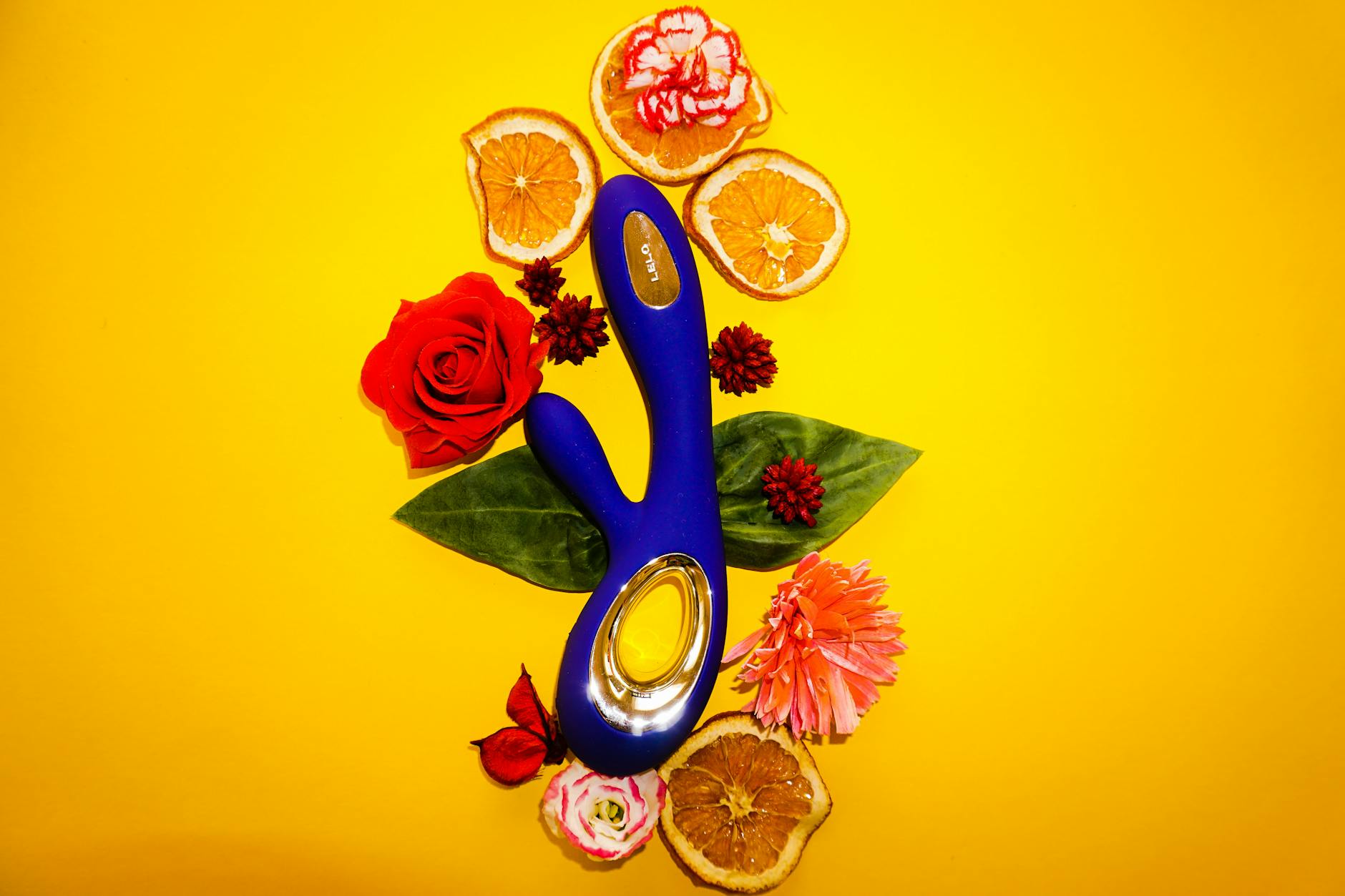 A blue clitoral vibrator surrounded by fresh citrus slices on a bright yellow background.