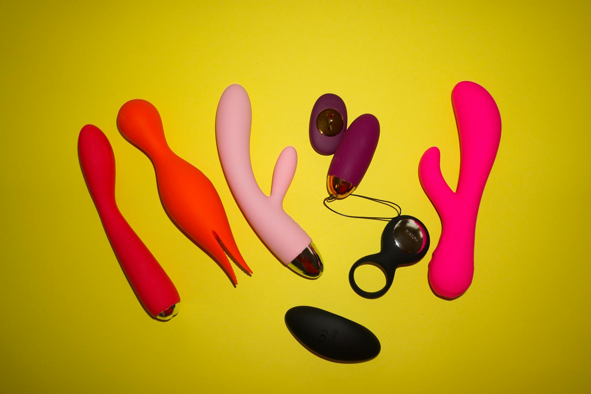 Colorful clitoral vibrators and suction toys arranged on a bright yellow background