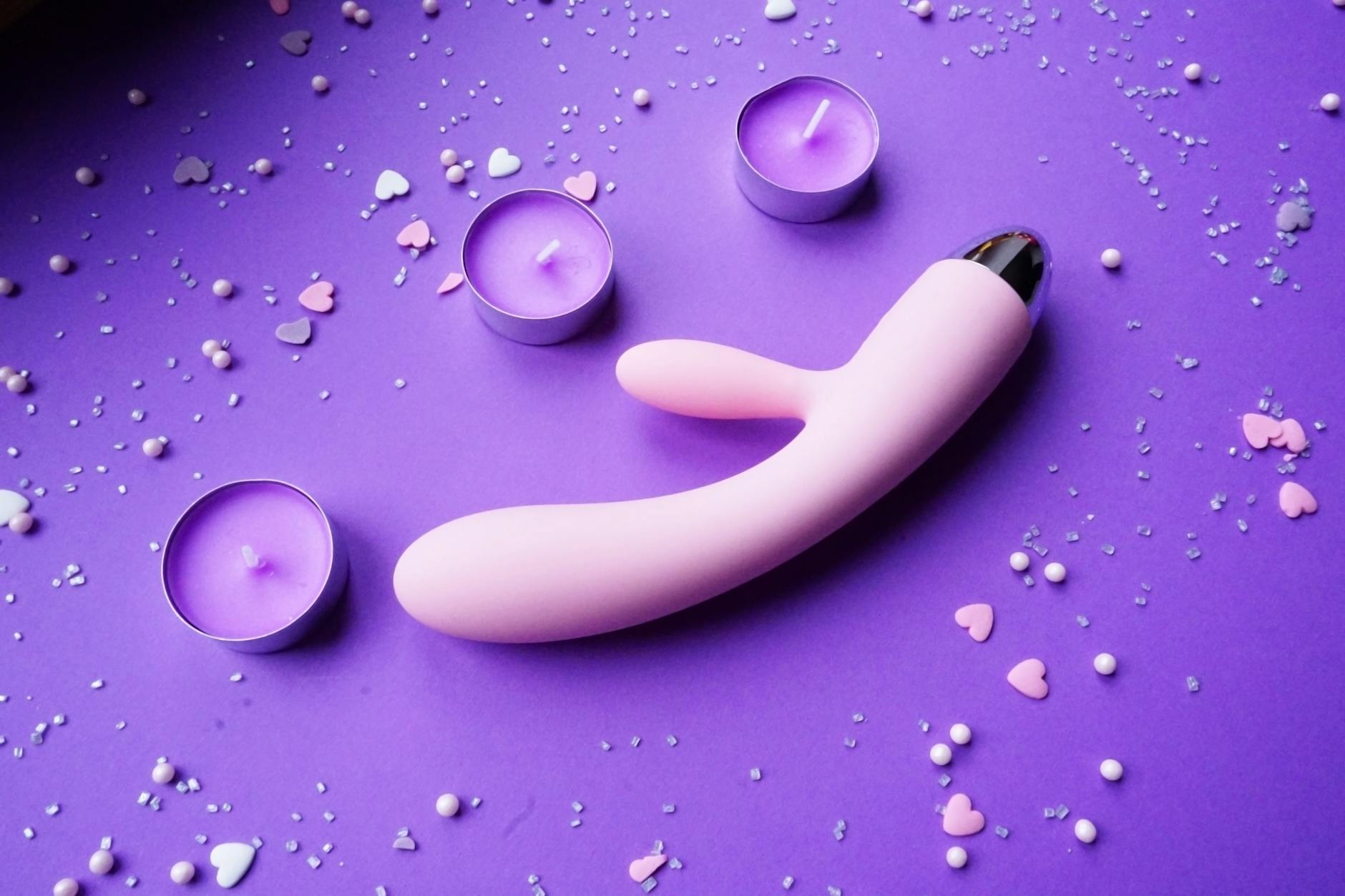 Pink lemon vibrator on purple background with heart confetti and candles for romantic intimacy